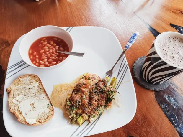Toast spread with cream cheese, a bowl of baked beans and a crumb-topped bake of asparagus and greens