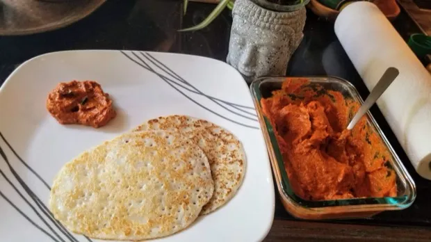 Two thin crisp dosas with a spoonful of red chutney and a dish of tomato-and-carrot chutney