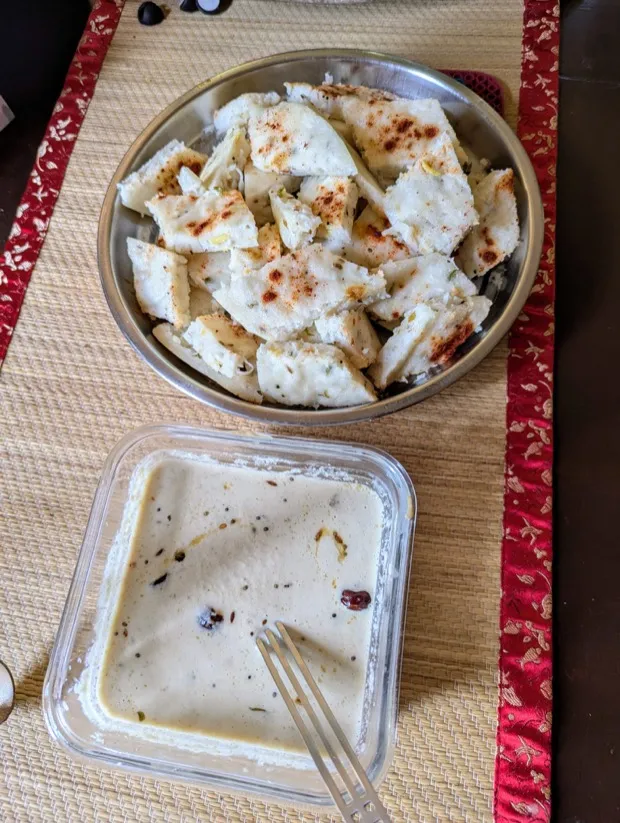 A steel bowl of idli wedges dusted with chilli powder, with a dish of coconut chutney alongside