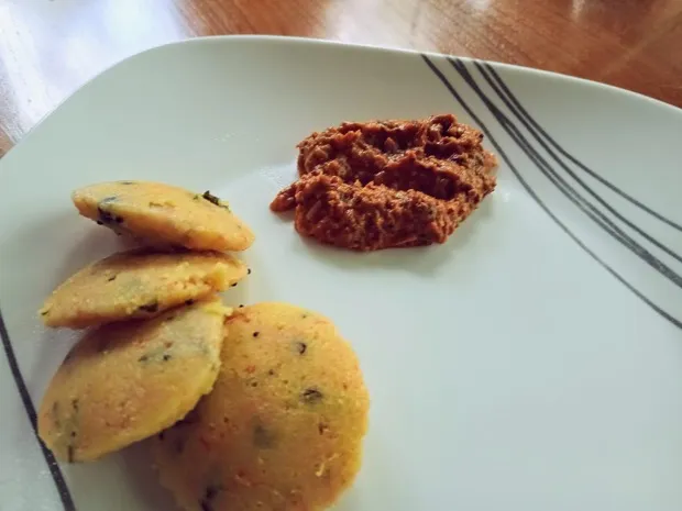 Steamed savoury lentil idli flecked with curry leaves, with a spoonful of red coconut-chilli chutney