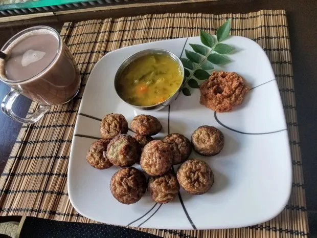 Paniyaram with a small bowl of vegetable kootu, a vadai and a sprig of curry leaves