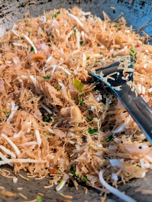 Vermicelli upma being tossed in a wok with cashews, curry leaves and coconut