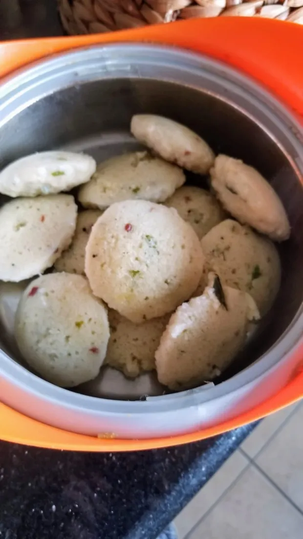 Freshly steamed idli, flecked with chilli and curry leaf, in an insulated container