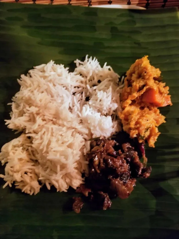 Steamed rice on a banana leaf with a spiced pumpkin curry and a dark greens fry