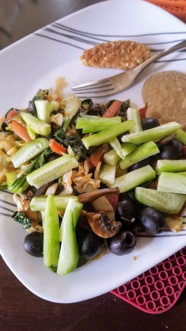 Stir-fried greens and mushrooms topped with fresh cucumber batons and black olives, with a cutlet and a millet flatbread