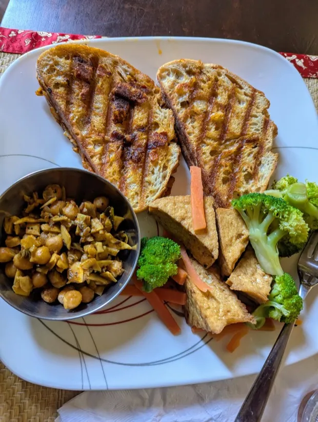 Grilled sourdough with a bowl of chickpea and jackfruit curry, pan-fried tofu, carrot batons and steamed broccoli
