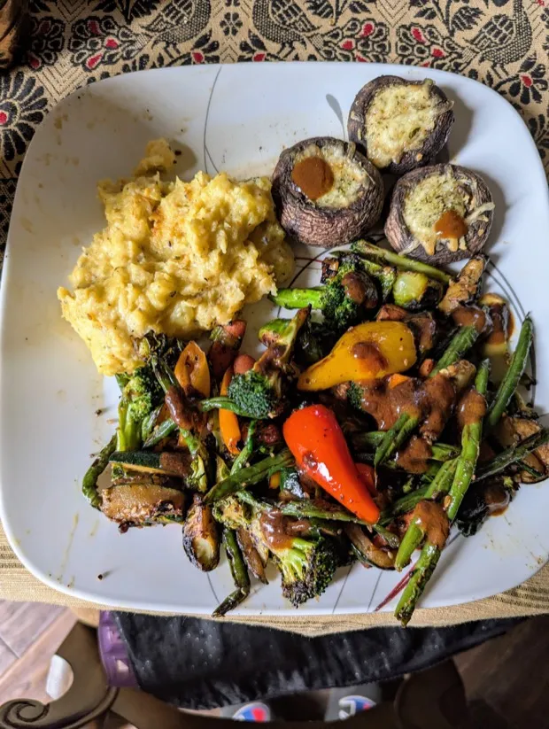 Mash served with cheese-topped mushroom caps and roasted vegetables with sweet mini peppers under a peanut sauce