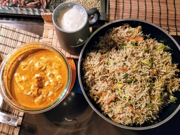 A bowl of paneer masala beside a large bowl of vegetable fried rice with peas, carrot, corn and broccoli