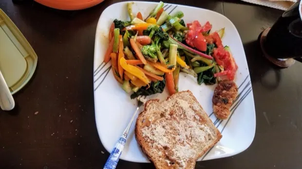 Stir-fried peppers, broccoli, carrots and greens with fresh tomato, a spiced cutlet and a slice of seeded toast