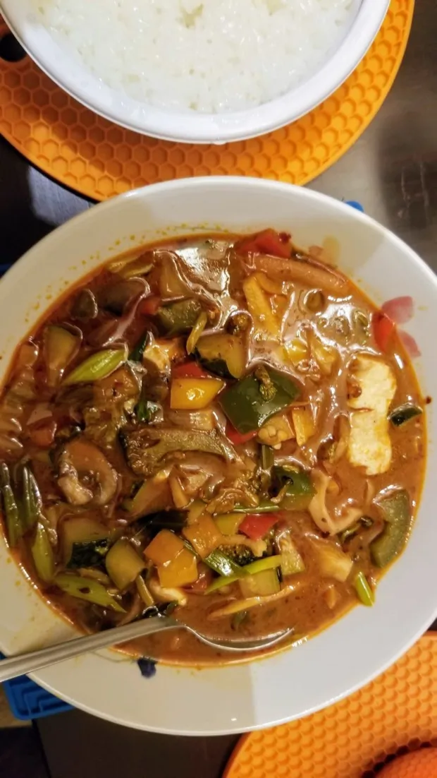 A bowl of red curry thick with peppers, courgette, mushrooms and tofu, with steamed rice alongside