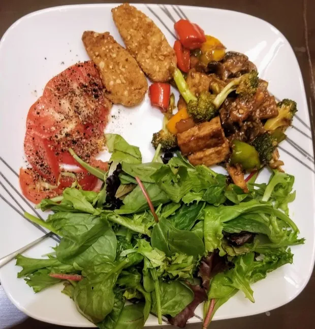 Peppered tomato slices and crumbed cutlets with a tofu-and-vegetable stir-fry and a generous pile of mixed baby leaves