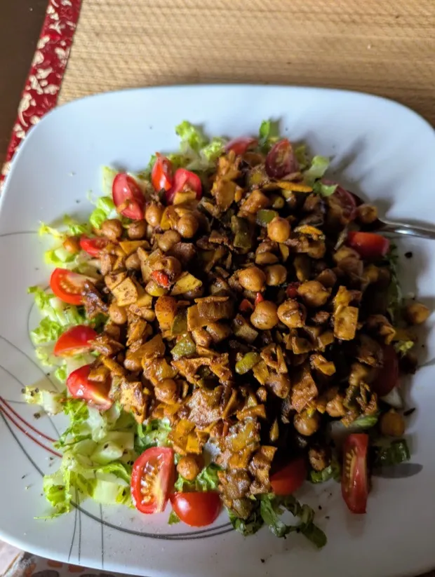 A chopped lettuce salad with halved cherry tomatoes under a spiced chickpea and jackfruit topping