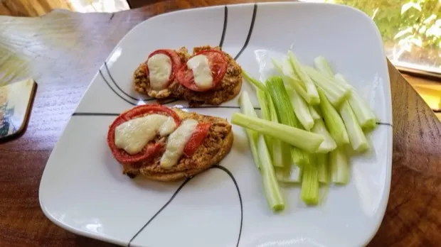 Toasted muffin halves topped with tomato and melted cheese, with celery sticks alongside