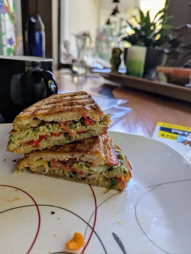 A pressed pesto-and-vegetable panini cut in half and stacked, layered with peppers, cucumber and paneer