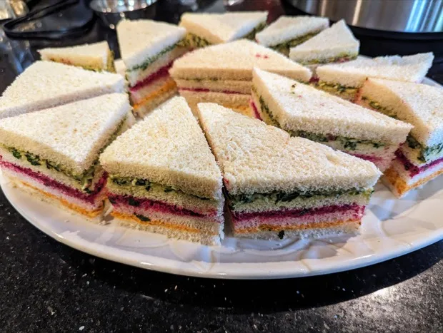 A platter of layered tea sandwiches cut into triangles — striped green with herb chutney, pink with beetroot and orange with carrot