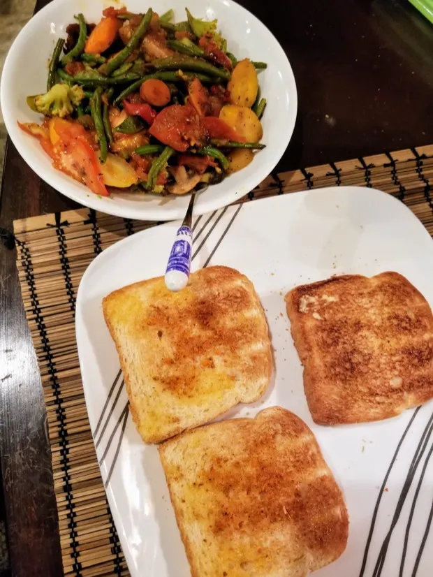 A bowl of green bean, carrot and tomato stir-fry with three slices of buttered toast dusted with chilli