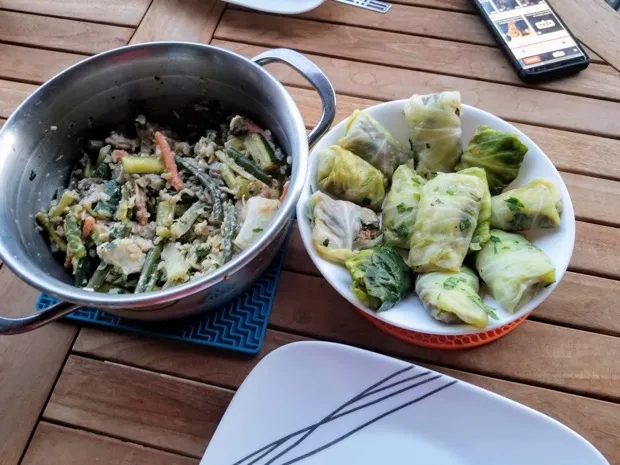A pan of green bean and vegetable stir-fry with a bowl of steamed cabbage rolls