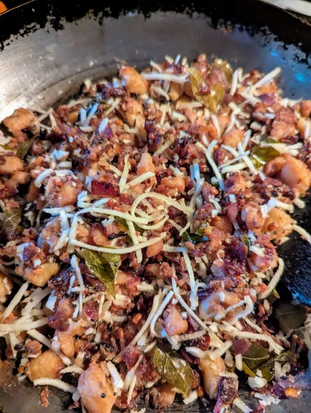 A stir-fry of golden root-vegetable pieces with mustard seeds, curry leaves and shredded coconut in a steel wok