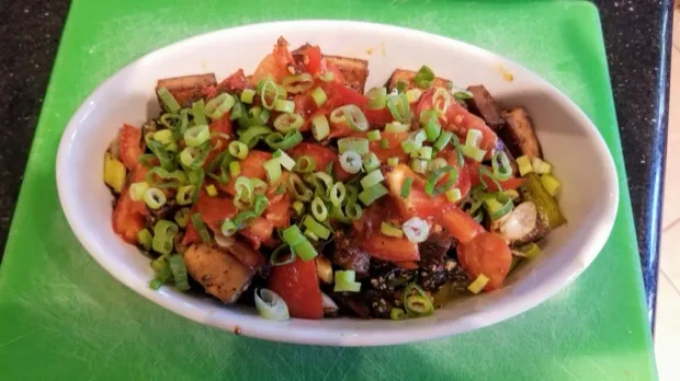 A dish of tofu and tomato stir-fry scattered with sliced spring onion