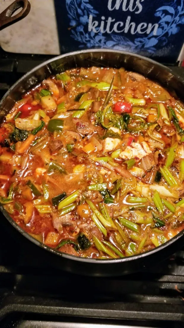 A wide pan of vegetable stew on the stove — celery, peppers, greens and paneer in a tomato broth